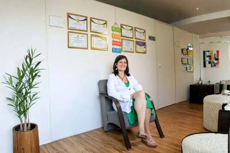 Valéria sentada ao lado das certificações da Clínica Integrativa Alpherat