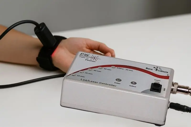 Close da aplicação de ILIB no pulso com o equipamento ativo sobre a mesa.